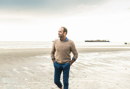 Mature man with hands in pockets contemplating while standing against sea during sunset