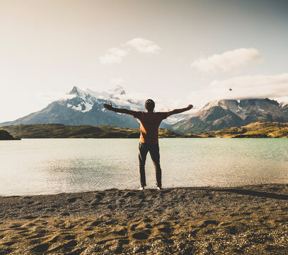 Man standing with arms outstretched at lake Pehoe in Torres Del Paine National Park Patagonia, South America