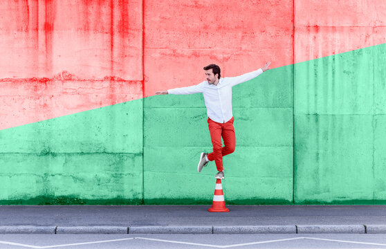 Carefree man standing on traffic cone against multi colored wall