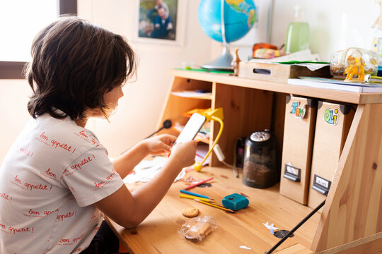 Boy sitting at desk at home using smartphone