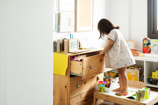 Cute girl searching in drawer while standing on table in playroom at home