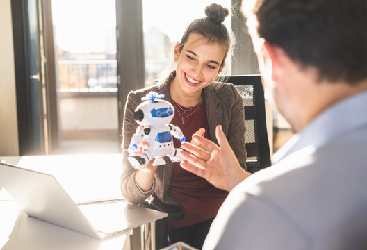 Young businesswoman showing robot toy to businessman while sitting at office