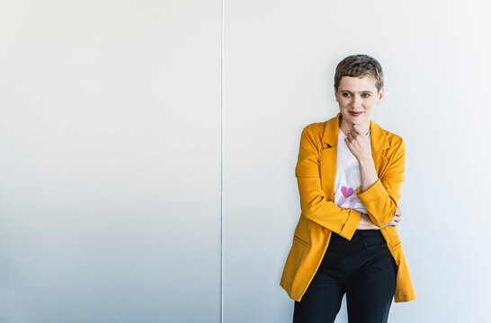 Thoughtful female entrepreneur wearing yellow blazer standing against wall in office
