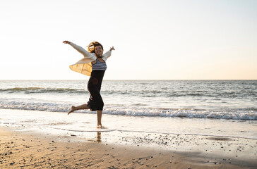 Carefree young woman running at beach against clear sky during sunset