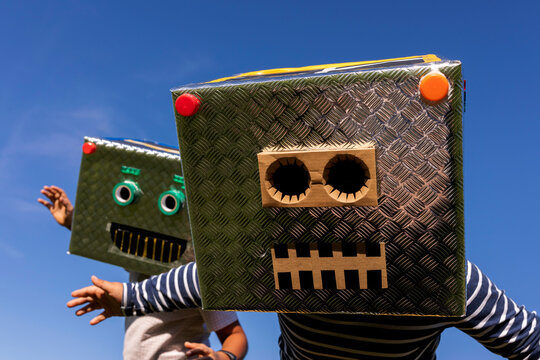 Brothers face covered with cardboard box playing against clear sky