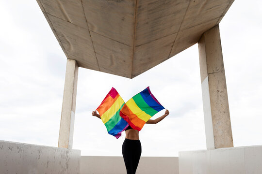 Mid adult woman waving rainbow flags while standing on built structure against sky