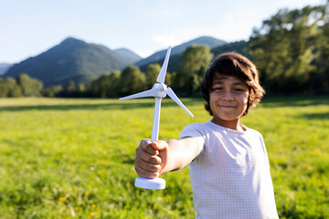 Smiling boy holding wind turbine toy while standing in meadow