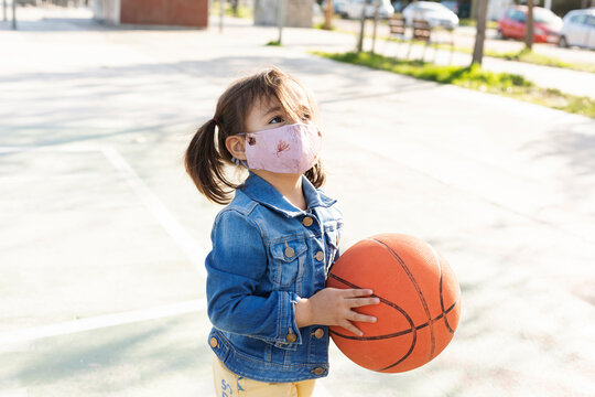 Portrait of little girl with basketball wearing protective mask