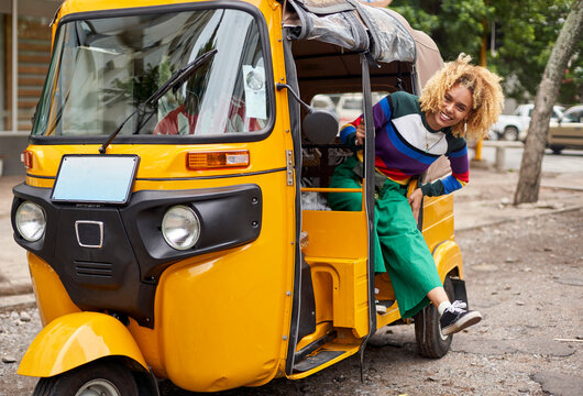 Full length portrait of smiling young woman leaning out from tuk-tuk in city