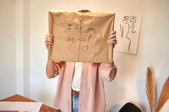 Female freelancer showing wrapped delivering package against wall at home