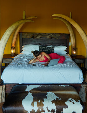 Woman lying on bed in hotel room using laptop