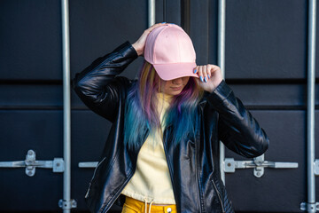 Portrait of young woman with dyed hair and baseball cap in front of black container