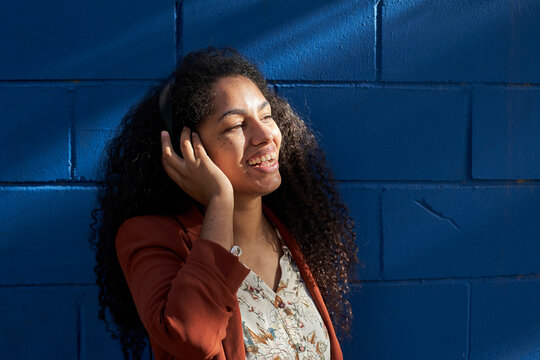 Woman wearing headphones looking away while standing against blue wall