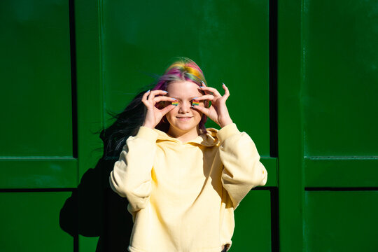 Portrait of young woman with dyed hair and rainbow candies in front of green container
