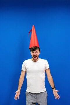 Cheerful male professional wearing cone shaped megaphone on head against blue wall in office