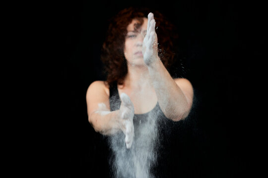 Woman clapping hands covered in white dust against black background