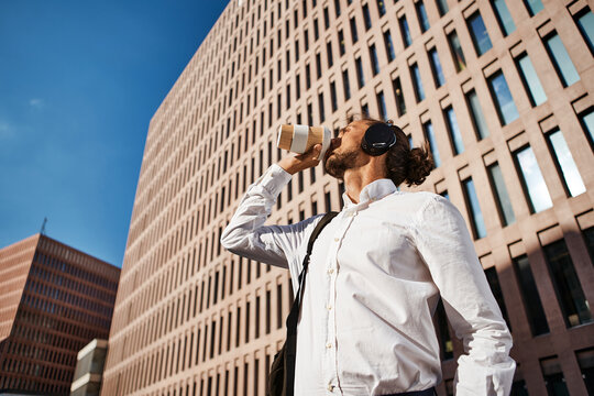 Businessman drinking coffee while listening to music against office building