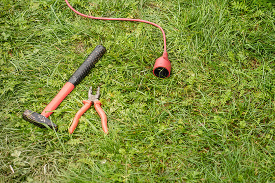 Extension cord, hammer and pliers lying on green grass