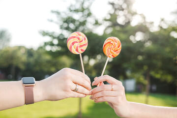 Hands of female friends holding lollipops at park