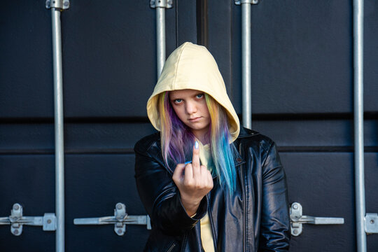 Portrait of young woman with dyed hair giving the finger in front of black container