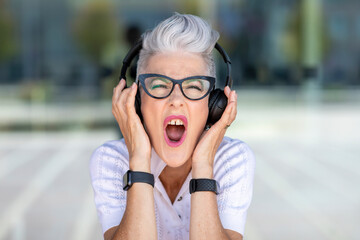 Excited senior woman screaming while listening to music through headphones