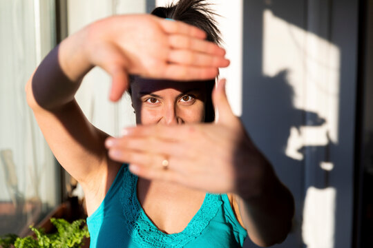 Woman standing by window, looking through finger frame
