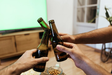 Hands of male friends toasting beer bottles at home