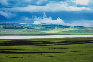 Georgia, Samtskhe-Javakheti, Poka, Green grassy plateau with lake and hills in background