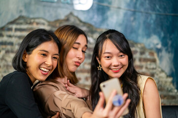 Group of Beautiful Asian woman friends meeting and using smartphone taking selfie together in cafe. Smiling female girlfriends enjoy weekend activity lifestyle at coffee shop together with happiness.