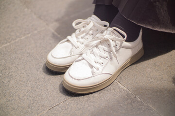 a woman wearing a black skirt is also wearing a pair of white shoes. she steps on an old tile floor.