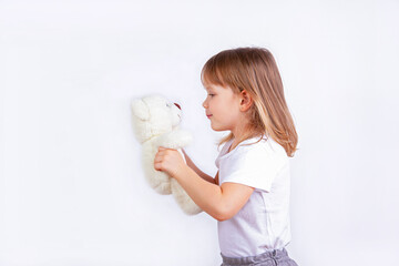 A cute little girl holds a teddy bear in her hands and looks at it.