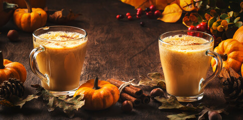 Pumpkin butter latte or coffee, keto drink on wooden table with fallen leaves, small pumpkins, pine...