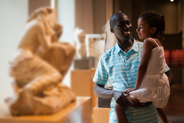 Portrait of African American man and his daughter at hall of Art Museum among exhibits of antiquity