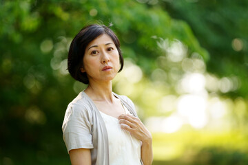 緑の中で遠くを見る中年女性　緑の中に立つミドル女性