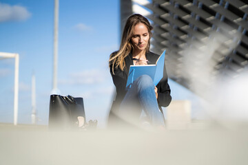 Businesswoman sitting on a wall taking notes