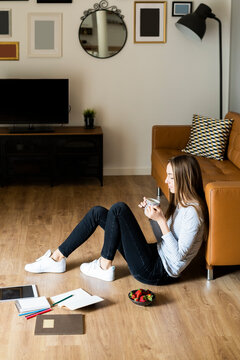 Relaxed young woman sitting on the floor at home drinking coffee