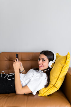 Young woman lying on the couch at home with smartphone and headphones