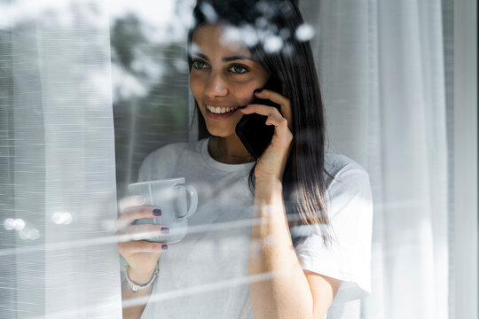 Smiling young woman on cell phone behind windowpane