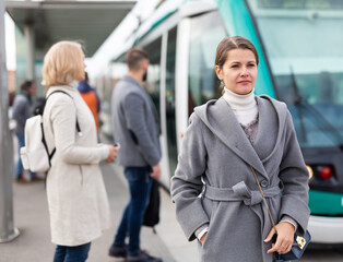 Fototapeta na wymiar Portrait of young woman waiting for tram at city public transport stop in autumn day..