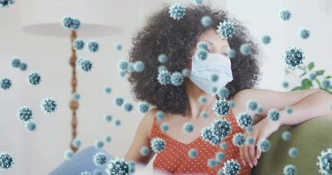Animation of coronavirus cells over african american woman wearing face mask at home