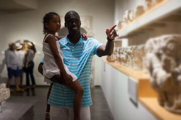 African American man and his little daughter looking at exhibits of antique sculpture at historical...
