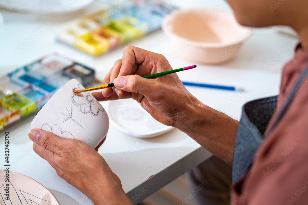 Wall mural asian lgbtq guy learning color painting her self-made pottery at home. confidence male enjoy hobbies