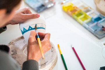Asian woman learning color painting her self-made pottery at home. Confidence female enjoy hobbies and indoors leisure activity handicraft ceramic sculpture and painting workshop at pottery studio.