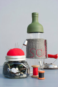 Mason jar with sewing buttons, pin cushion, spools of thread, thimble and bottle with embroidered felt cover