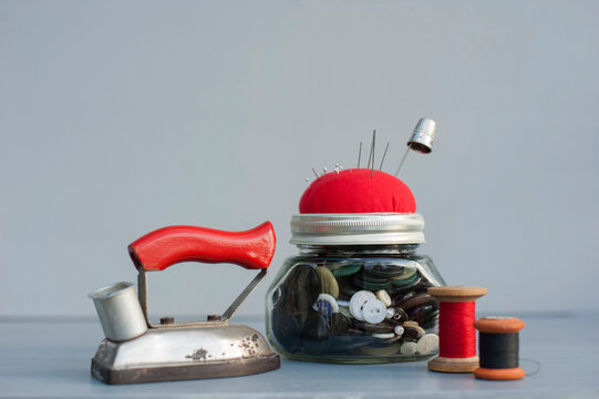 Mason jar with sewing buttons, pin cushion, spools of thread, thimble and retro iron