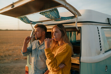 Couple brushing teeth at camper van in rural landscape at sunset