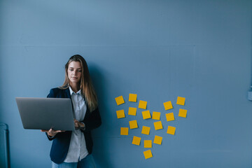 Young businesswoman using laptop with heart shape of sticky notes on the wall