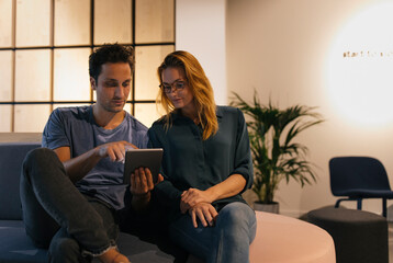 Young man and woman sitting on couch sharing tablet