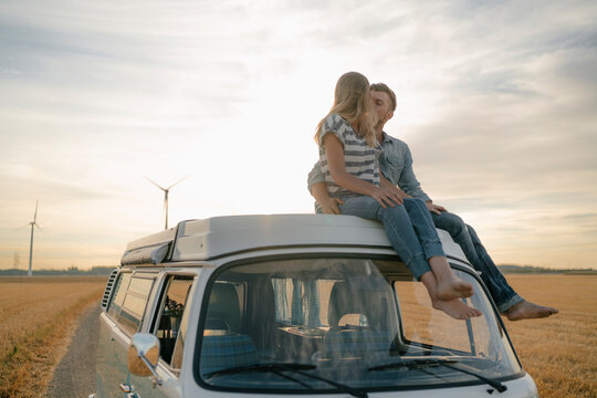 Couple kissing on roof of a camper van in rural landscape