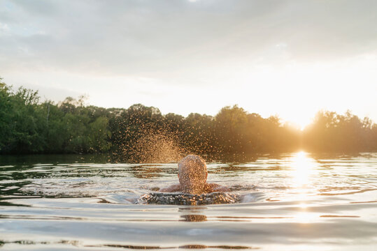 Senior man swimming in a lake at sunset